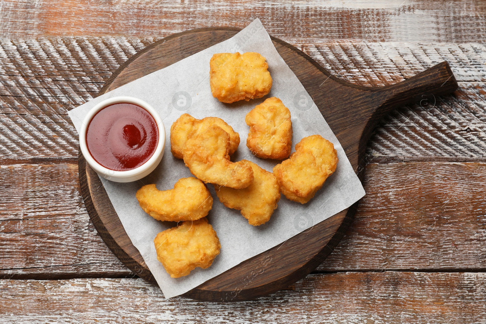 Photo of Delicious chicken nuggets and ketchup on wooden table, top view