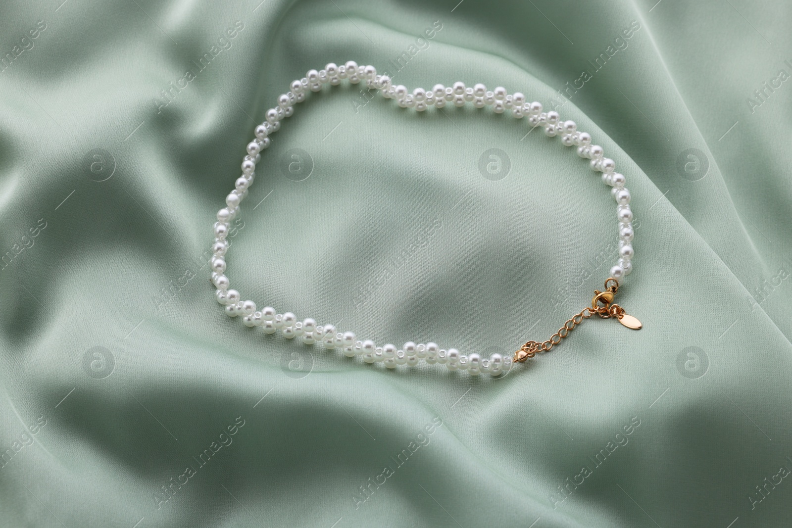 Photo of Beautiful pearl necklace on light green cloth, top view