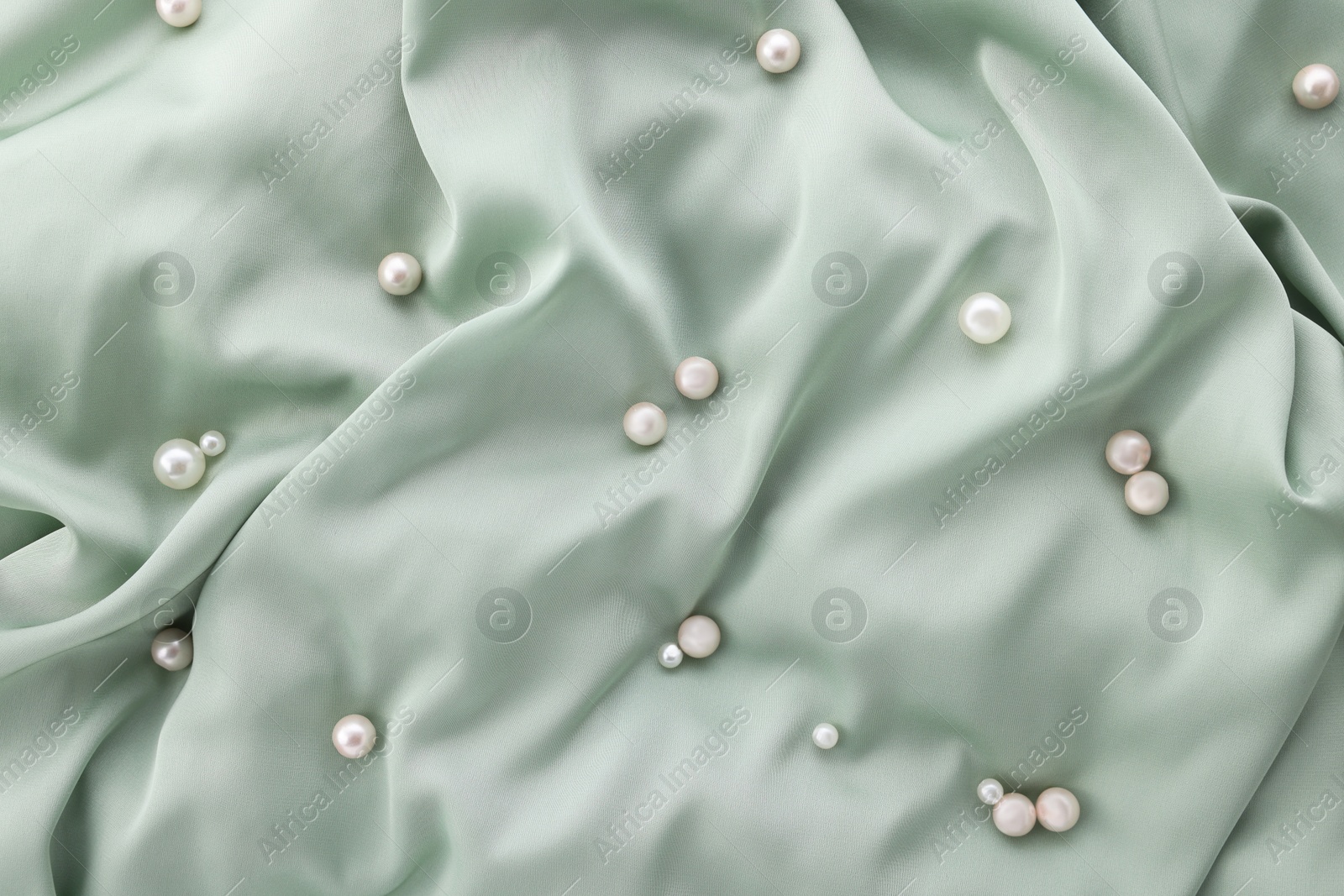 Photo of Many shiny pearls on light green cloth, top view