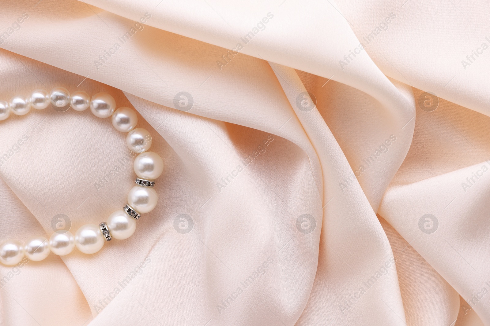 Photo of Beautiful pearl bracelet on beige cloth, top view. Space for text