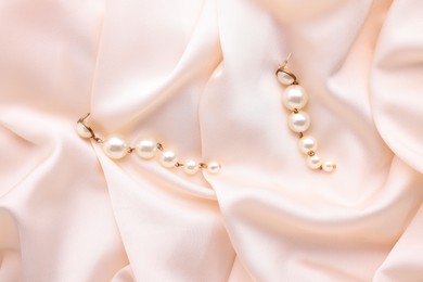 Photo of Beautiful pearl earrings on beige cloth, top view