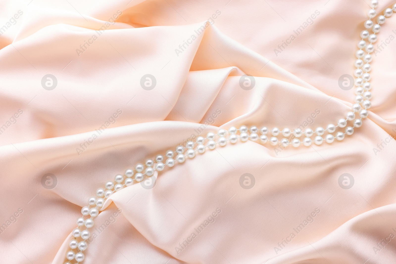 Photo of Beautiful pearl necklace on beige cloth, top view