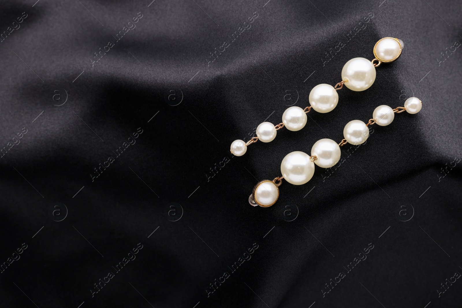 Photo of Beautiful pearl earrings on black cloth, top view. Space for text