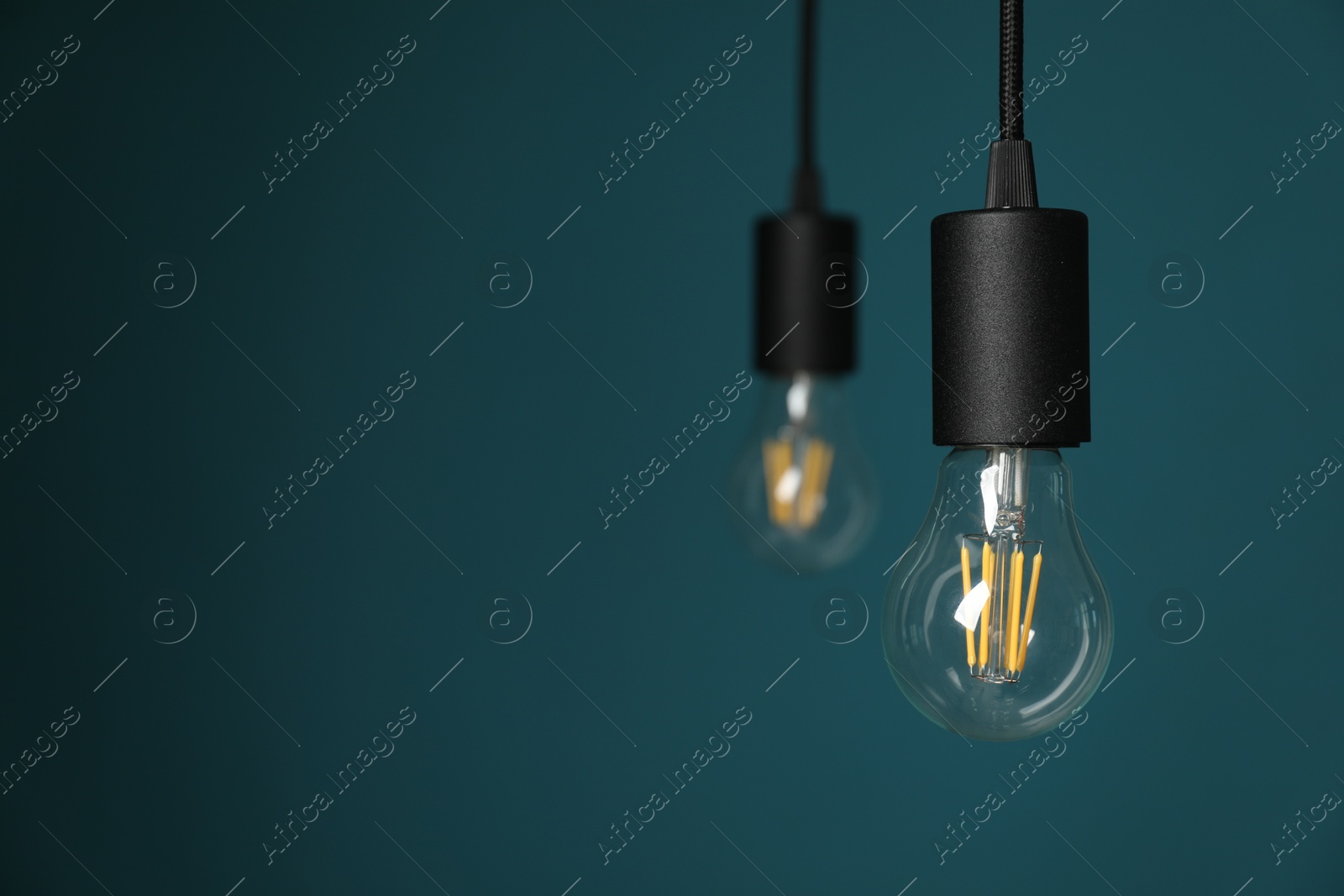 Photo of Light bulbs hanging on cords against teal background, selective focus. Space for text