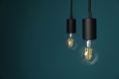 Photo of Light bulbs hanging on cords against teal background, selective focus. Space for text