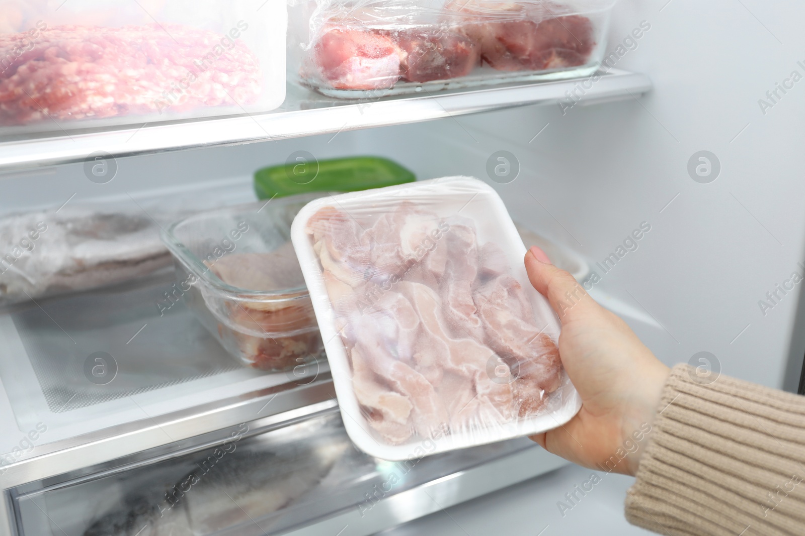 Photo of Woman taking frozen chicken meat out of fridge, closeup