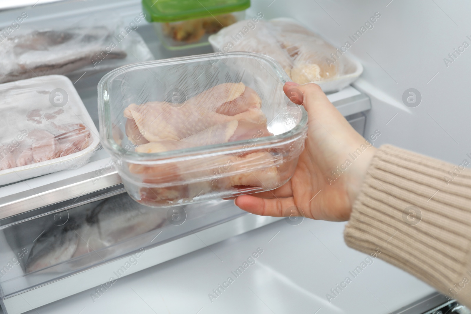 Photo of Woman taking frozen chicken drumsticks out of fridge, closeup