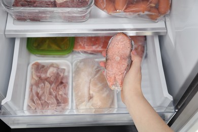 Photo of Woman taking frozen salmon steak out of fridge, closeup