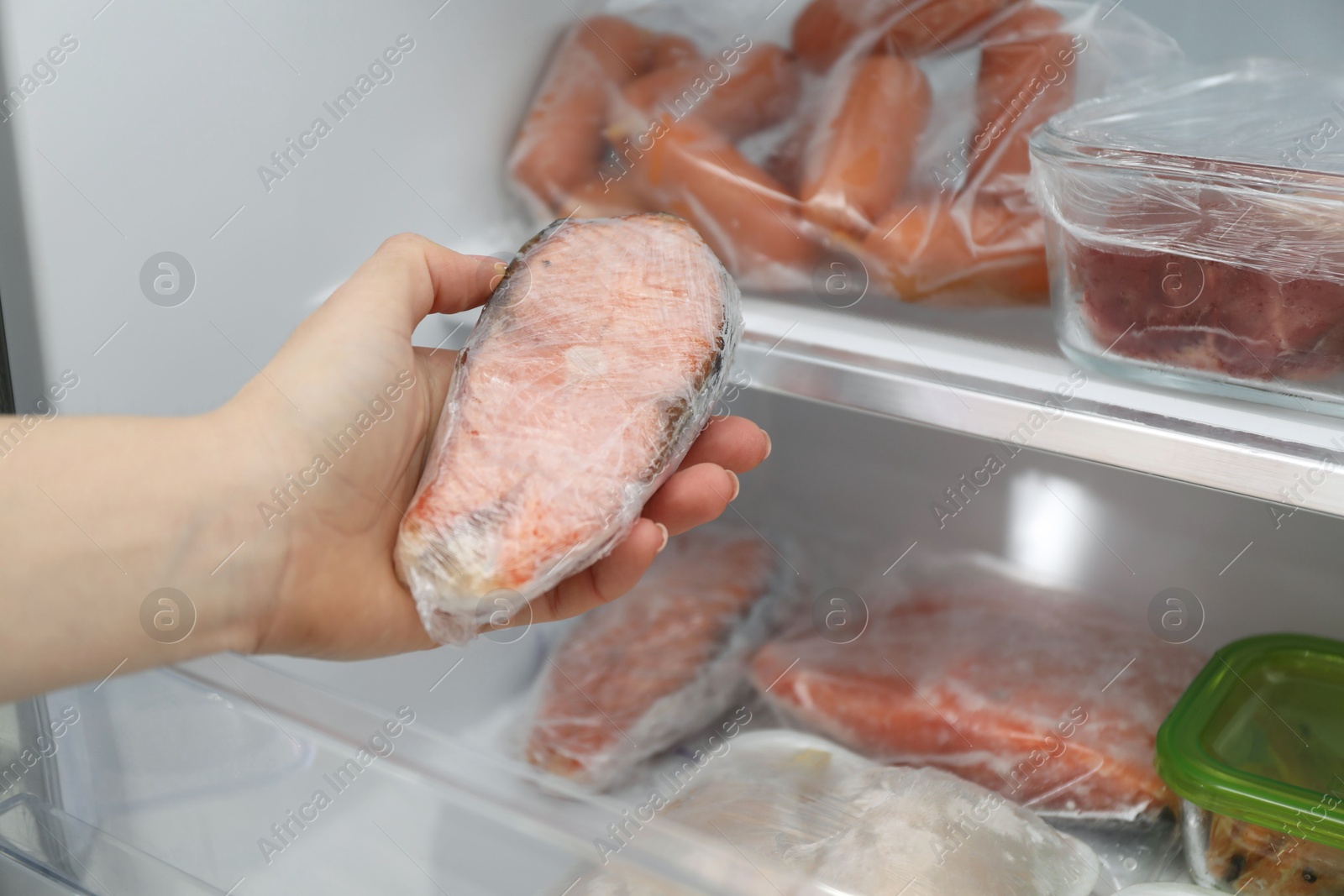 Photo of Woman taking frozen salmon steak out of fridge, closeup