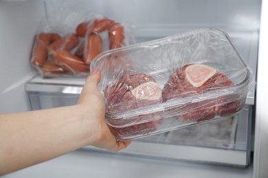 Photo of Woman taking frozen beef steaks out of fridge, closeup