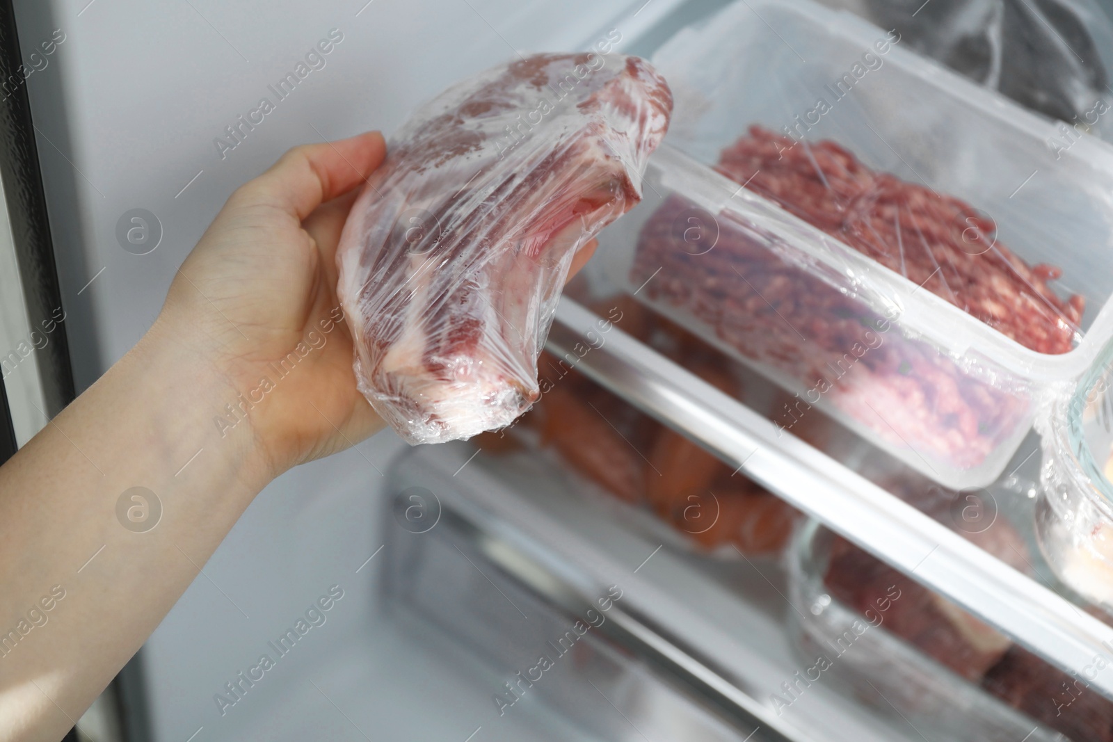 Photo of Woman taking frozen pork steak out of fridge, closeup