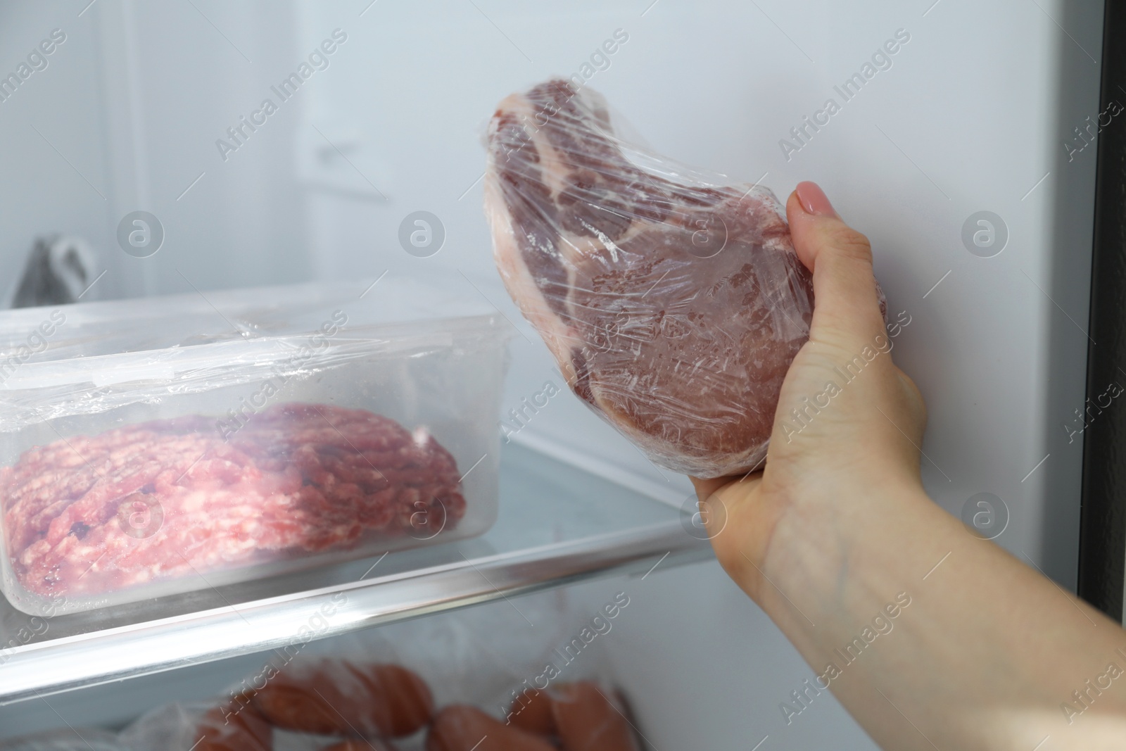 Photo of Woman taking frozen pork steak out of fridge, closeup