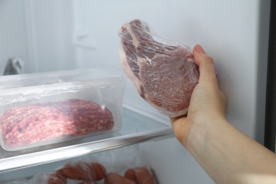 Photo of Woman taking frozen pork steak out of fridge, closeup