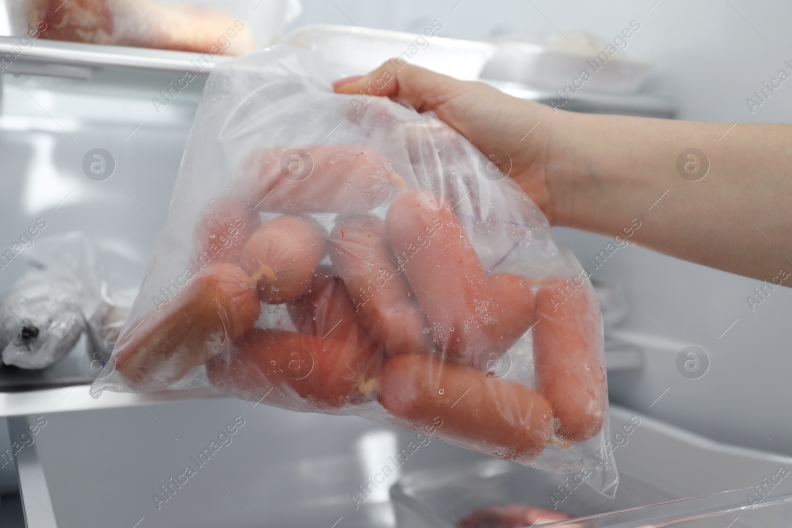 Photo of Woman taking bag of frozen sausages out of fridge, closeup