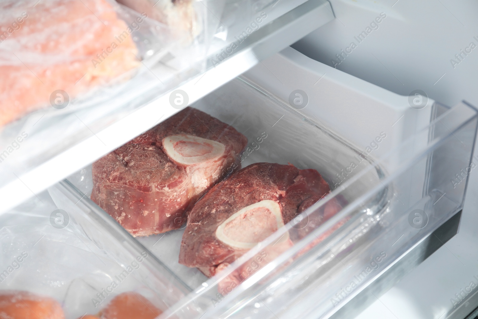 Photo of Frozen beef steaks in container of refrigerator, closeup