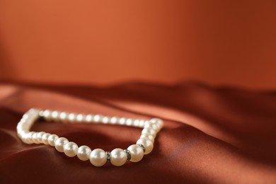 Photo of Beautiful pearl necklace on brown silk, closeup. Space for text