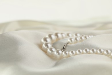 Photo of Beautiful pearl necklace on white silk, closeup