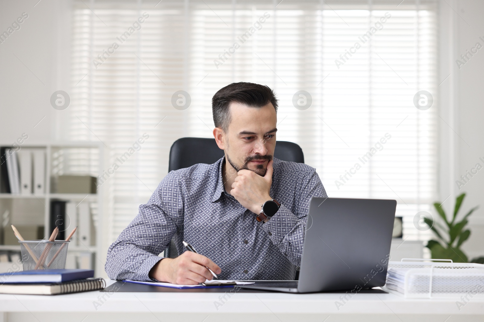 Photo of Handsome banker working with laptop at table in office