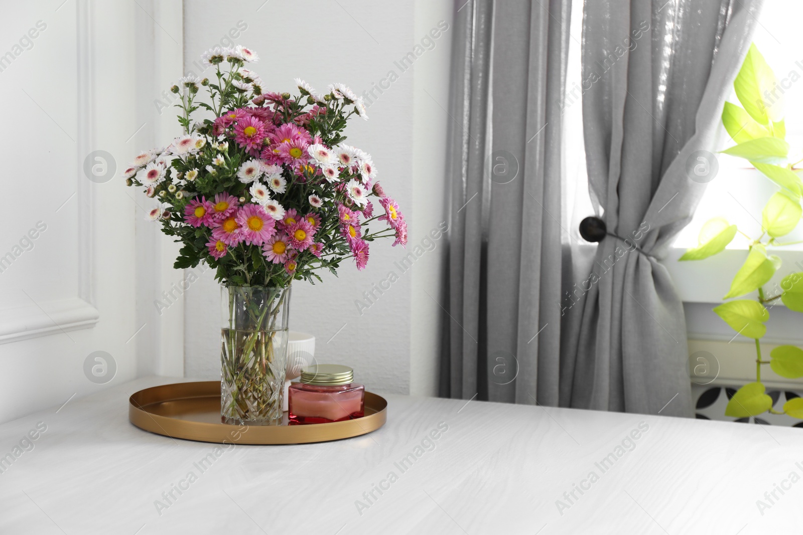 Photo of Beautiful flowers in vase and candles on white wooden table at home