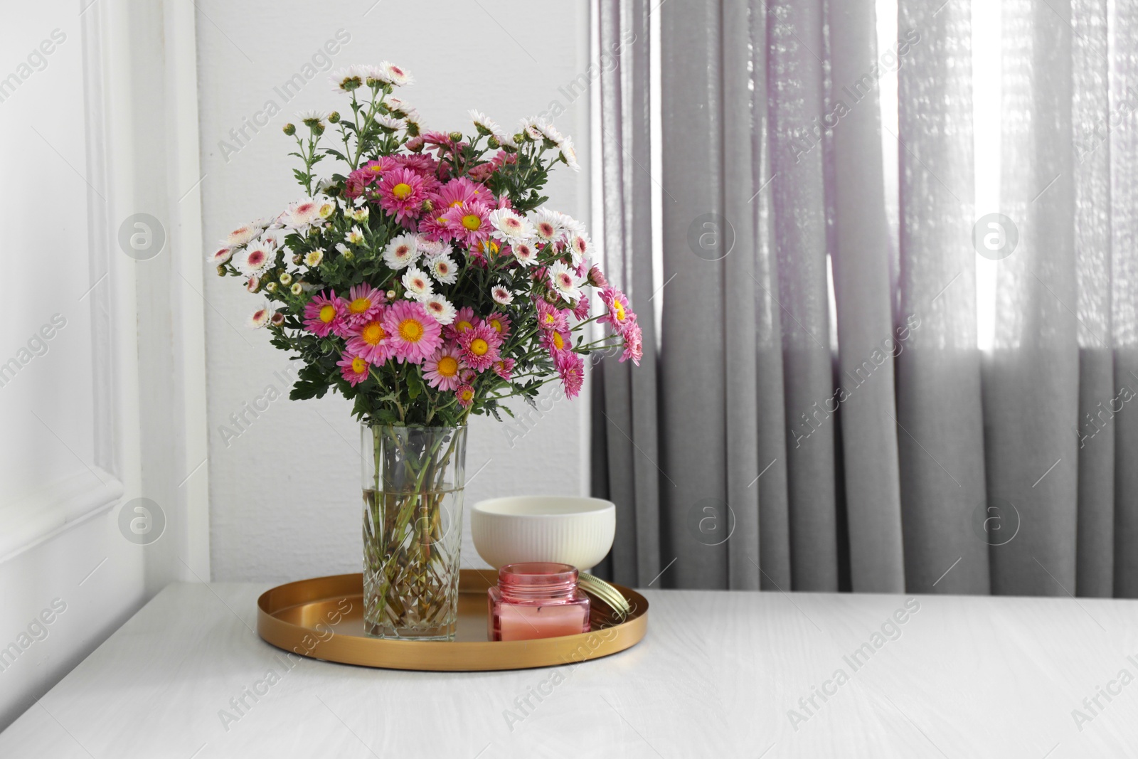 Photo of Beautiful flowers in vase and candles on white wooden table at home, space for text