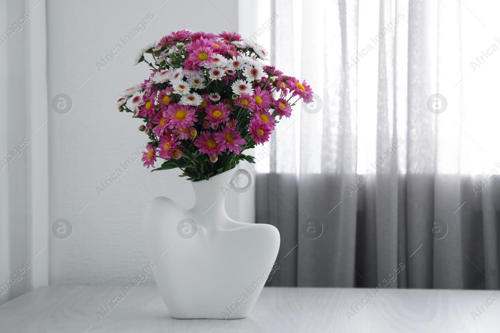 Photo of Stylish vase with beautiful flowers on white wooden table at home, space for text