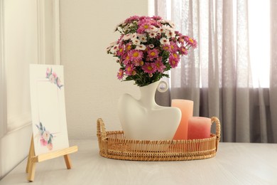 Photo of Stylish vase with beautiful flowers, candles and small easel on white wooden table at home