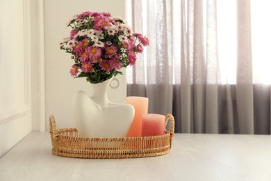 Photo of Stylish vase with beautiful flowers and candles on white wooden table at home, space for text