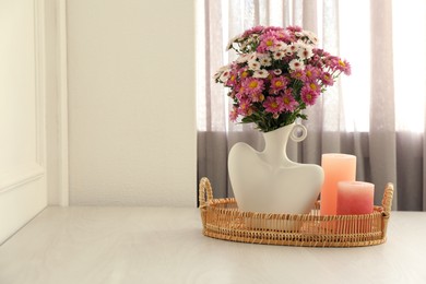 Photo of Stylish vase with beautiful flowers and candles on white wooden table at home, space for text