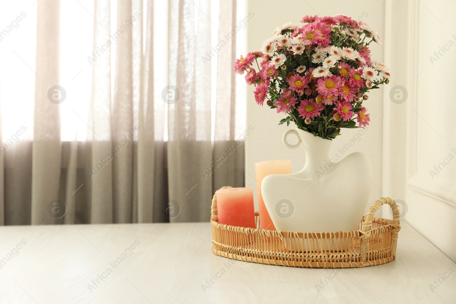 Photo of Stylish vase with beautiful flowers and candles on white wooden table at home, space for text