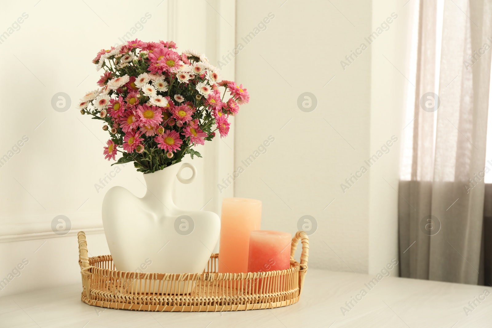 Photo of Stylish vase with beautiful flowers and candles on white wooden table at home, space for text