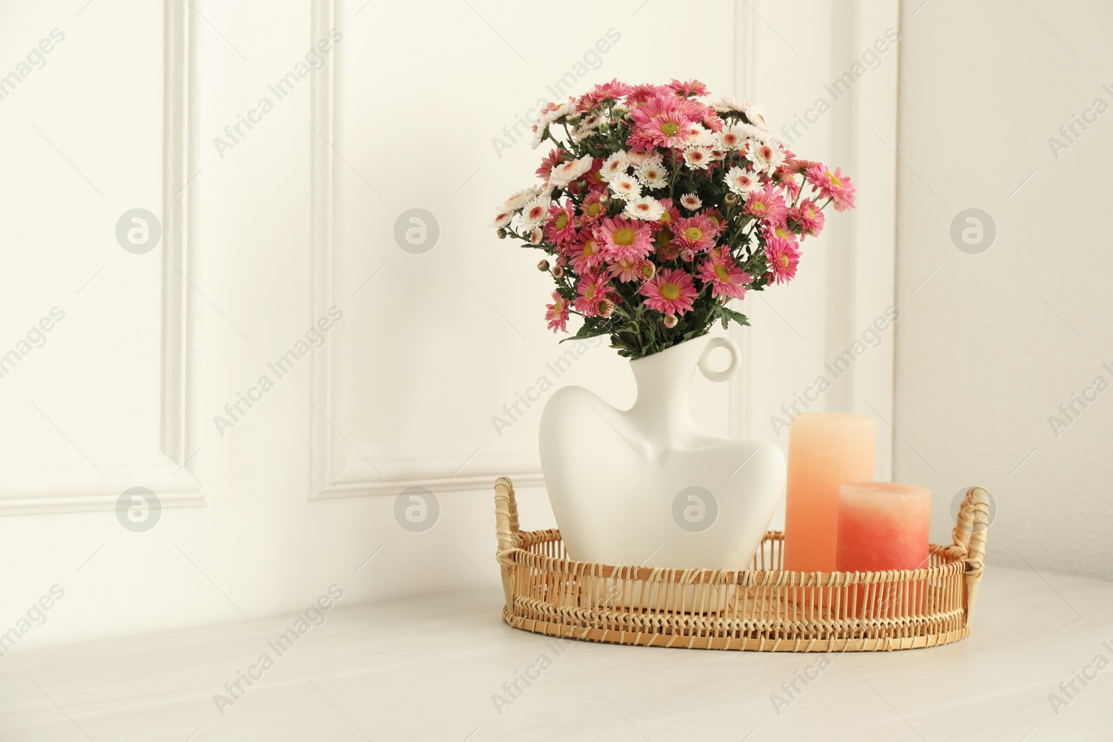 Photo of Stylish vase with beautiful flowers and candles on white wooden table at home, space for text