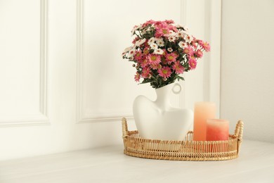 Photo of Stylish vase with beautiful flowers and candles on white wooden table at home, space for text