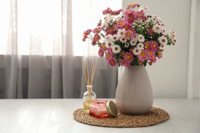 Photo of Beautiful flowers in vase, candle and reed diffuser on white wooden table at home, space for text