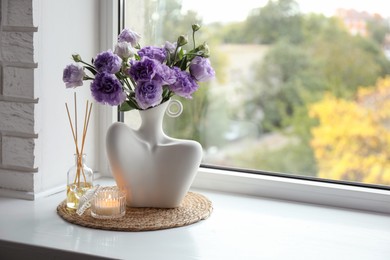 Photo of Stylish vase with beautiful flowers, candle and reed diffuser near window at home, space for text