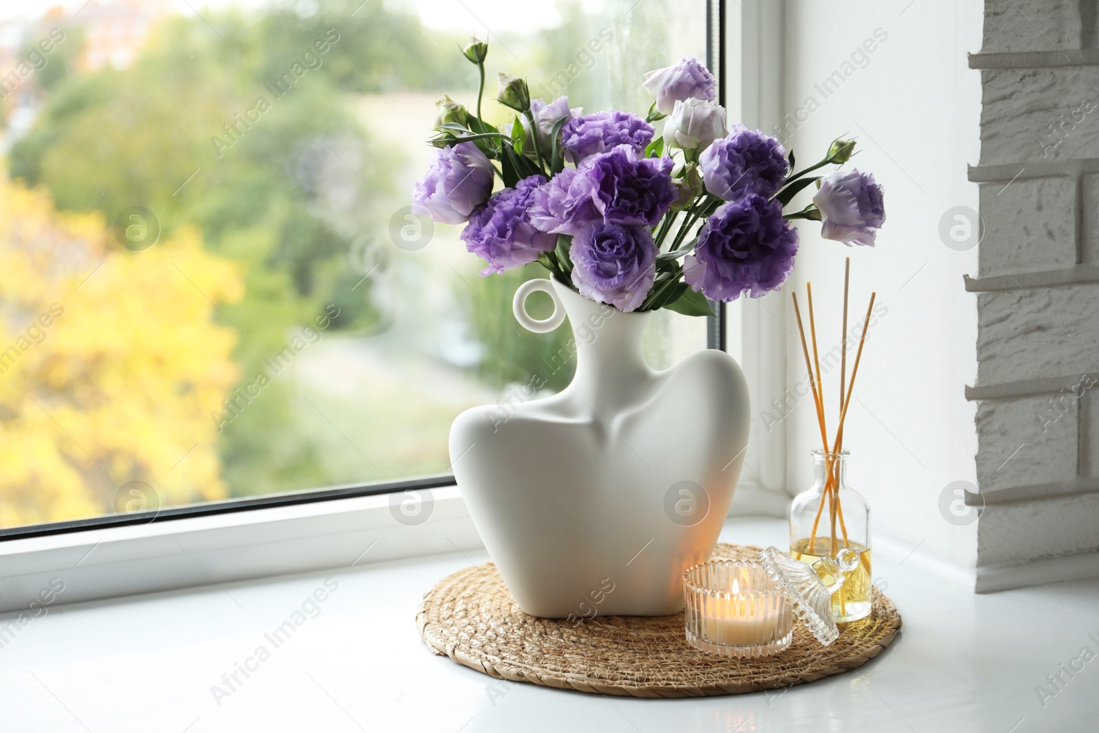 Photo of Stylish vase with beautiful flowers, candle and reed diffuser near window at home, space for text