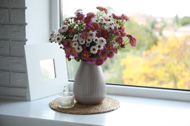 Photo of Beautiful flowers in vase and candle near window at home