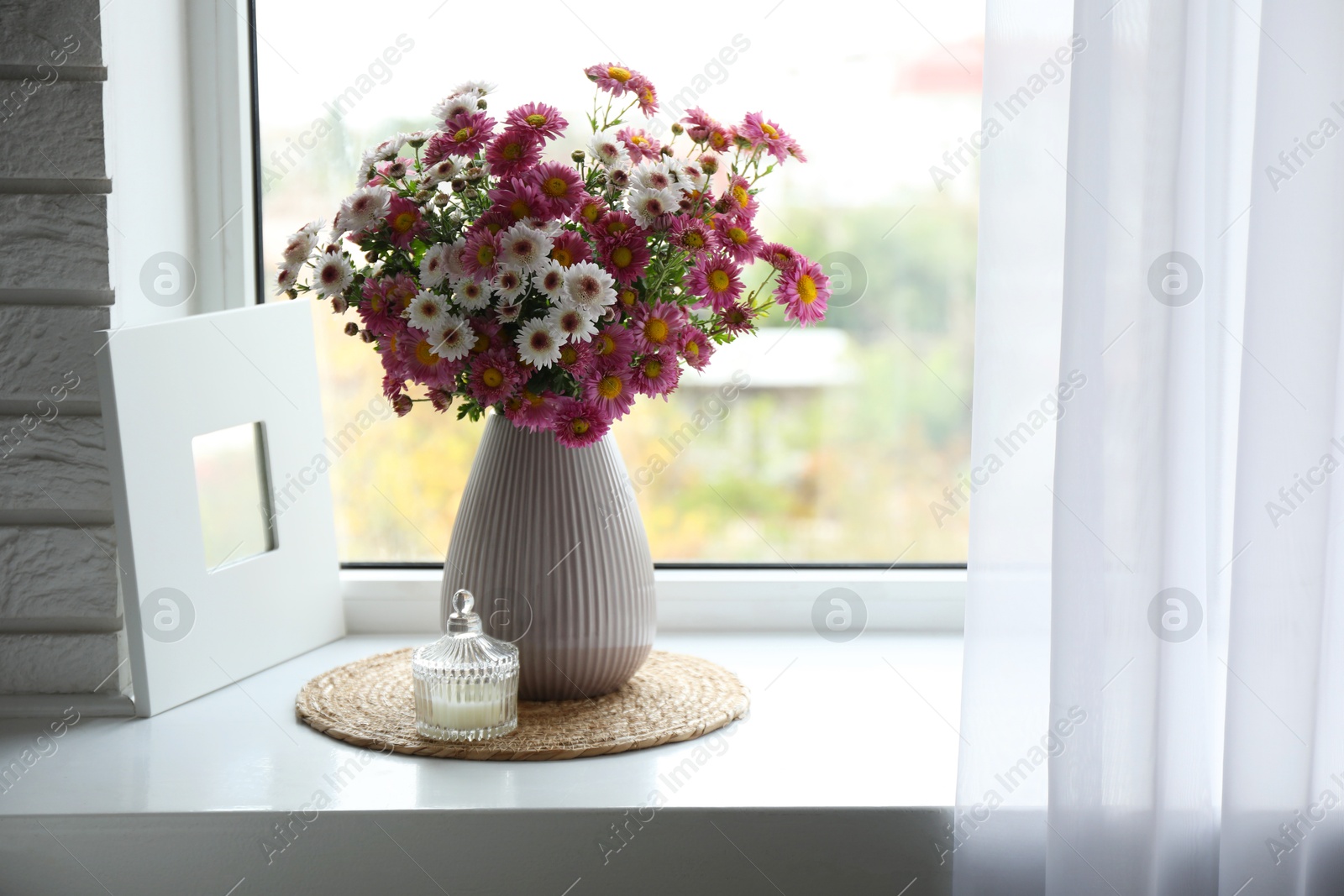 Photo of Beautiful flowers in vase and candle near window at home