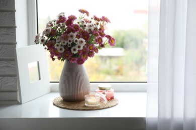 Photo of Beautiful flowers in vase and candles near window at home