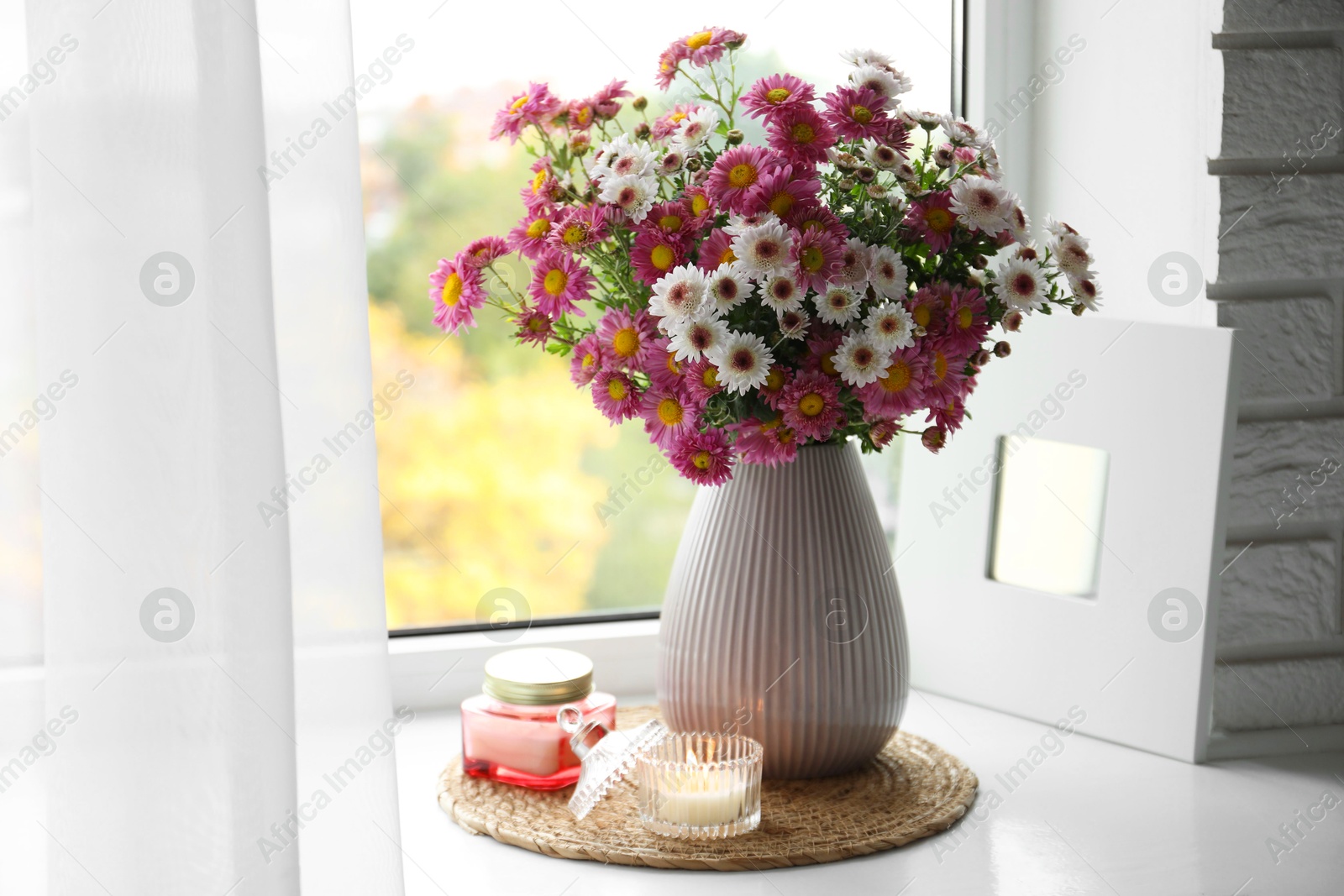 Photo of Beautiful flowers in vase and candles near window at home