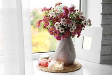 Photo of Beautiful flowers in vase and candles near window at home