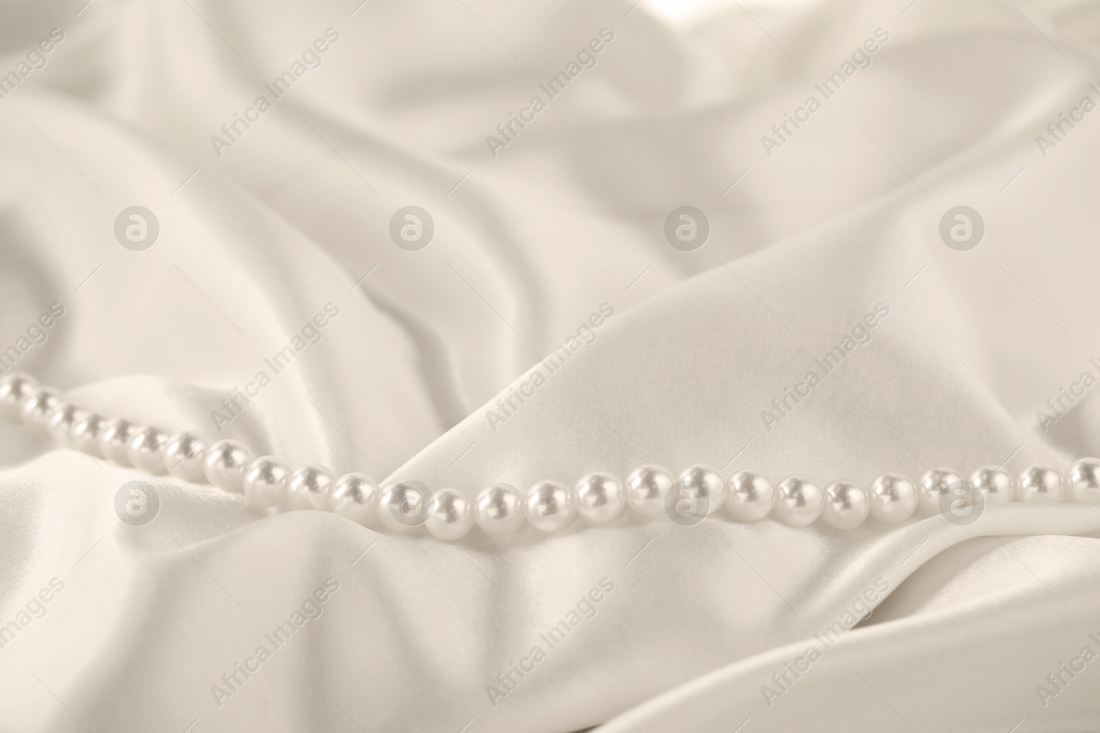 Photo of Beautiful pearl necklace on white silk, closeup. Space for text