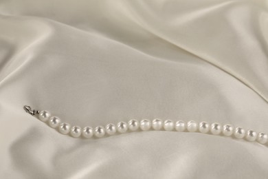 Photo of Beautiful pearl necklace on white silk, closeup. Space for text