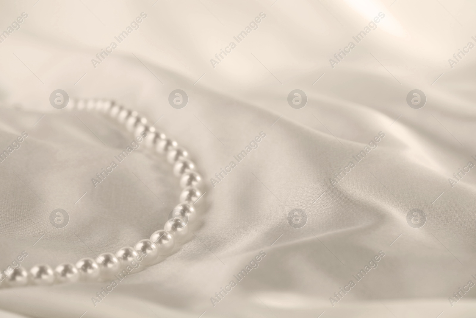 Photo of Beautiful pearl necklace on white silk, closeup. Space for text