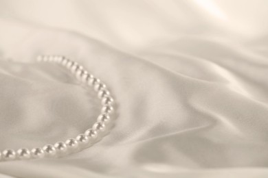 Photo of Beautiful pearl necklace on white silk, closeup. Space for text