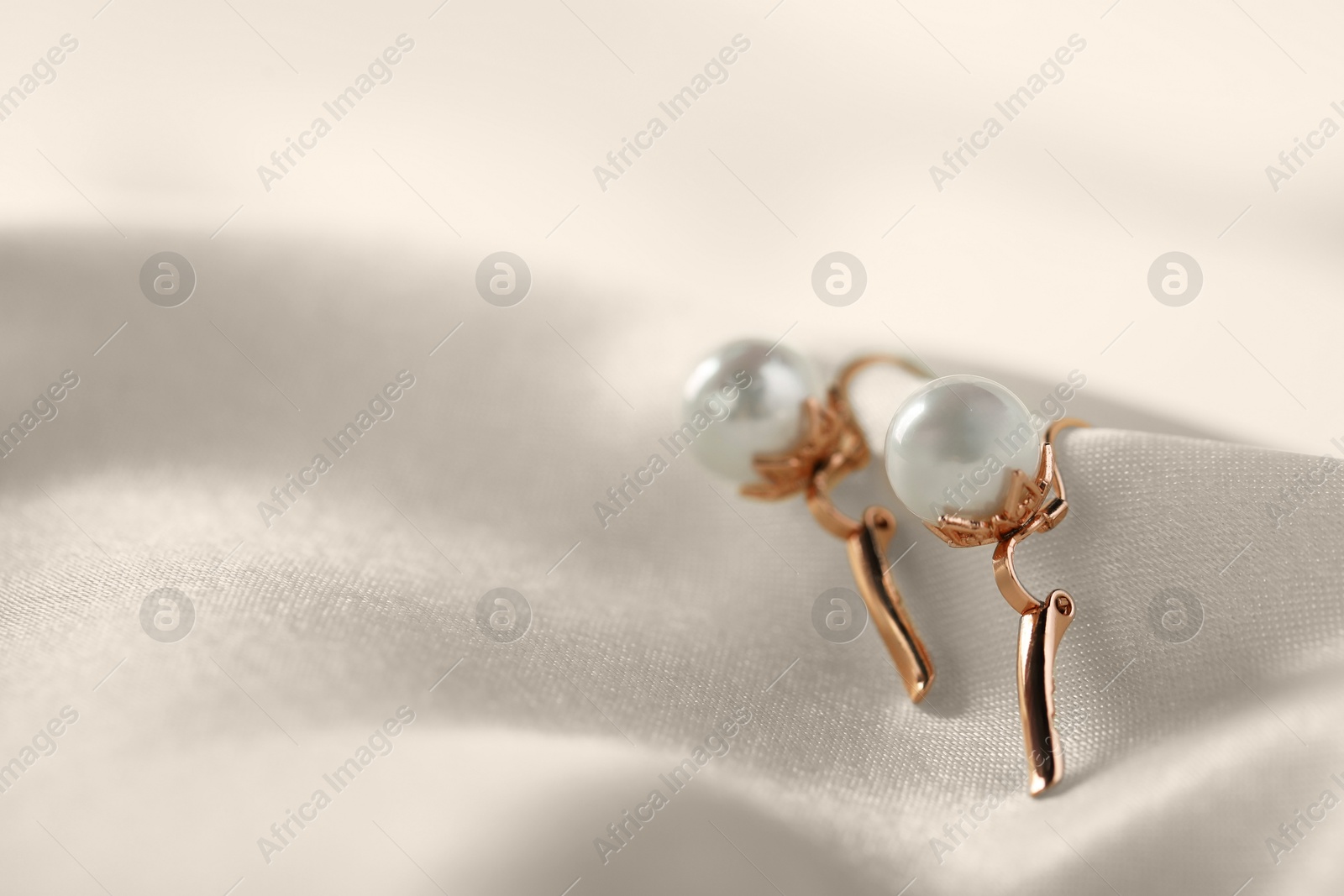 Photo of Beautiful pearl earrings on white silk, closeup. Space for text