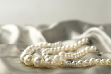 Photo of Beautiful pearl necklace on white silk, closeup