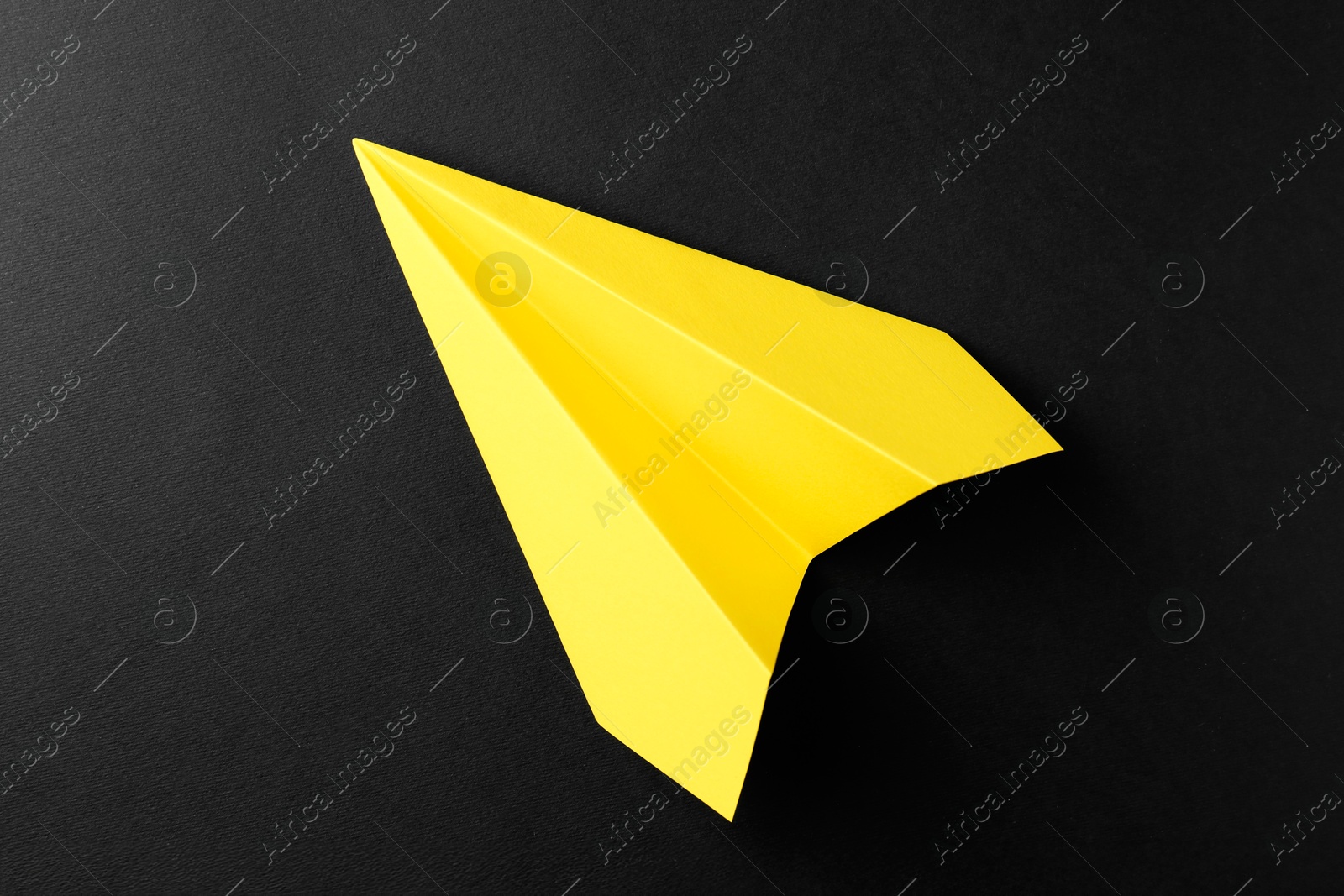 Photo of One handmade yellow paper plane on black background, top view