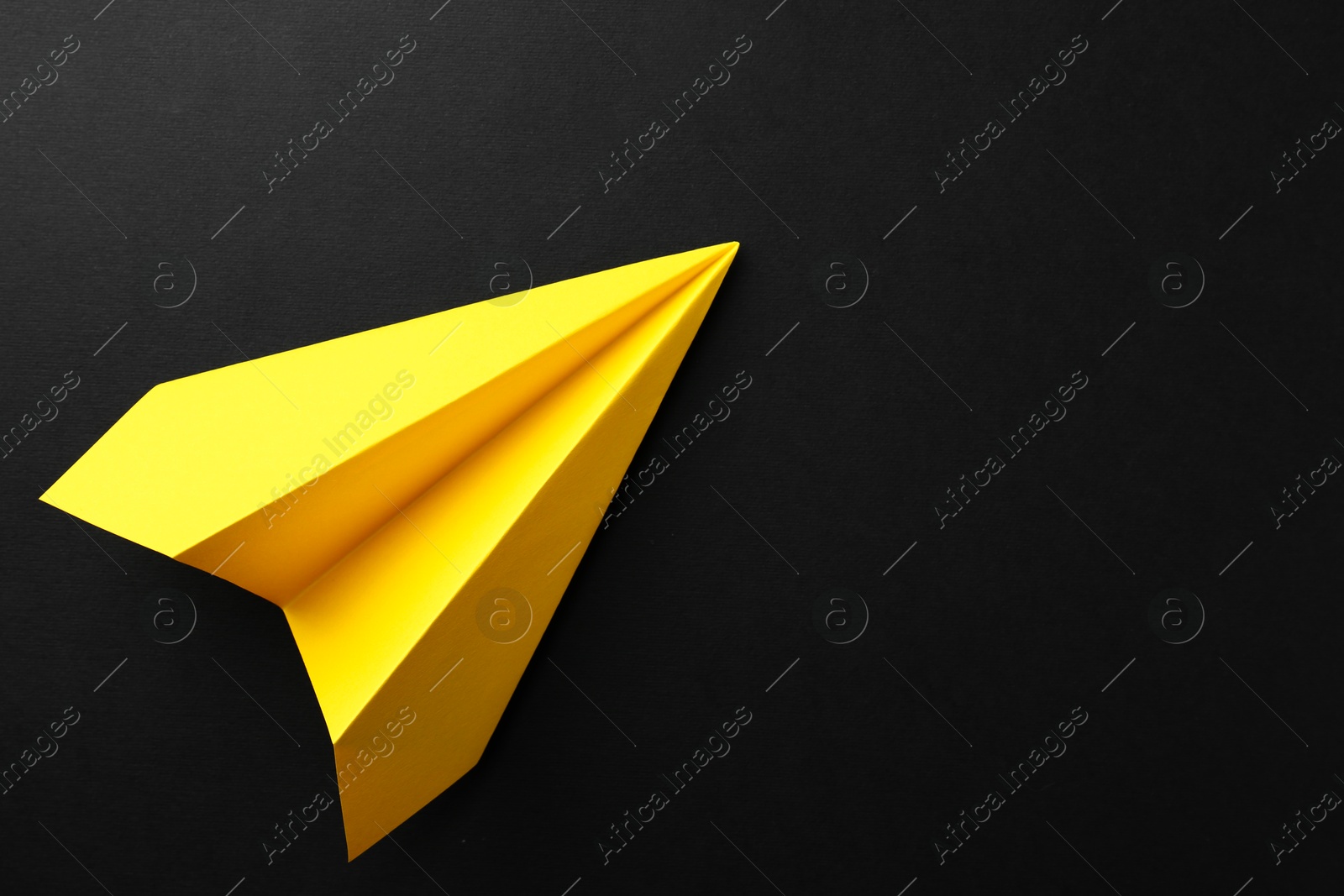 Photo of One handmade yellow paper plane on black background, top view. Space for text