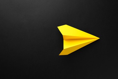 Photo of One handmade yellow paper plane on black background, top view. Space for text