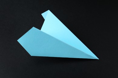 Photo of One handmade light blue paper plane on black background, closeup